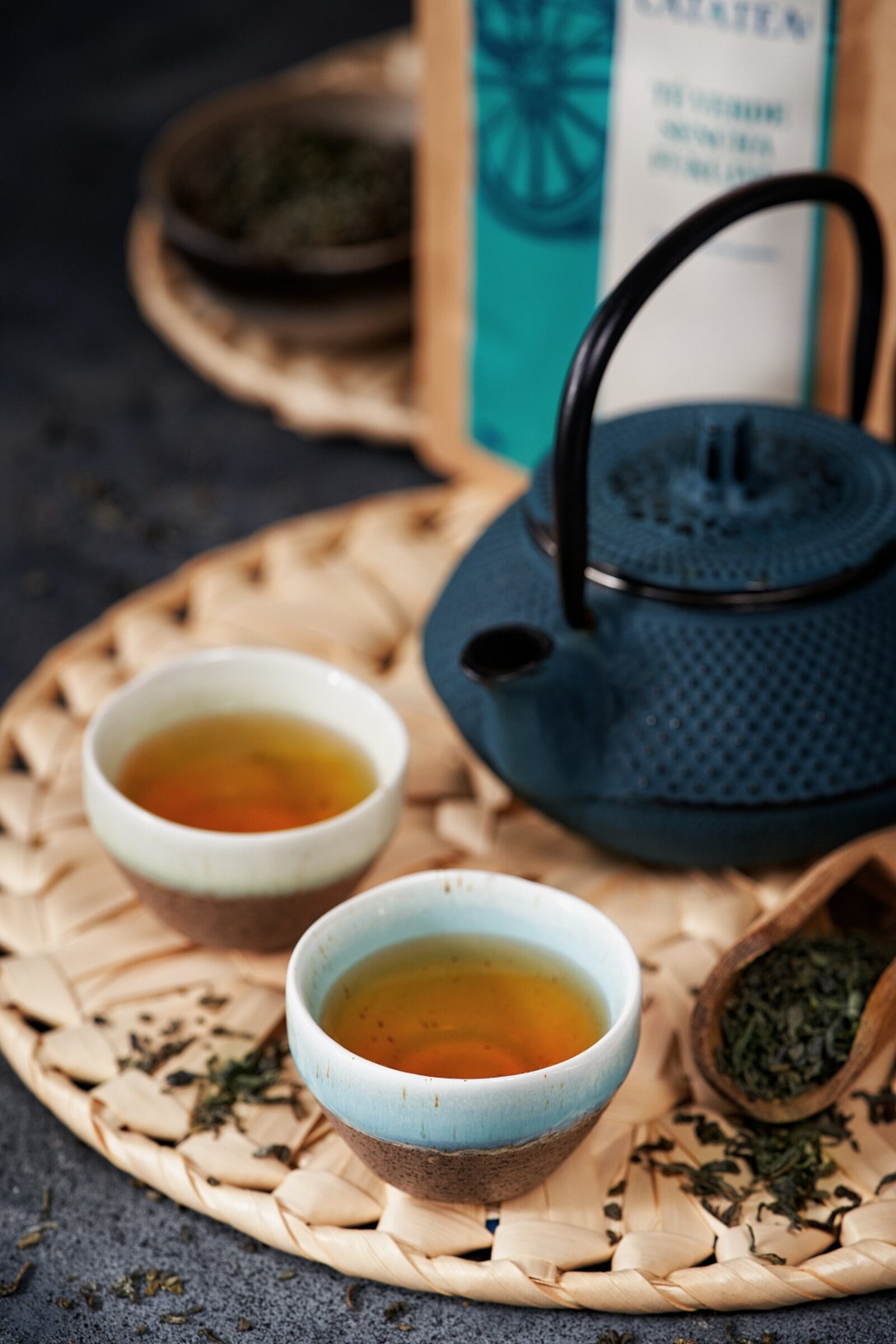 Tetera japonesa amb tasses de te i fulles sobre una safata de bambú